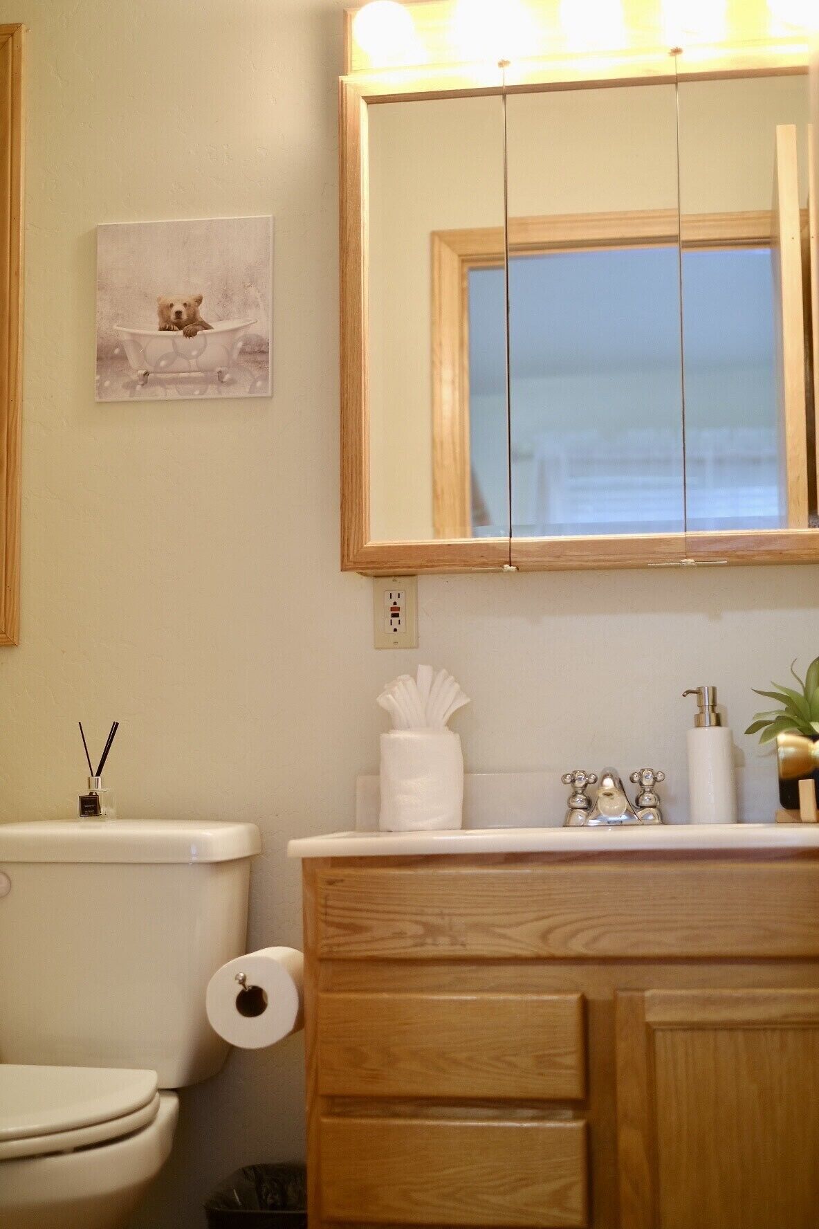 A bathroom with a wooden vanity, a toilet, a mirror, and a framed picture on the wall.