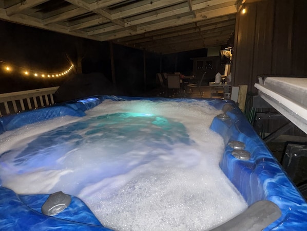 Un bain à remous avec un intérieur bleu et une terrasse en bois qui l’entoure.