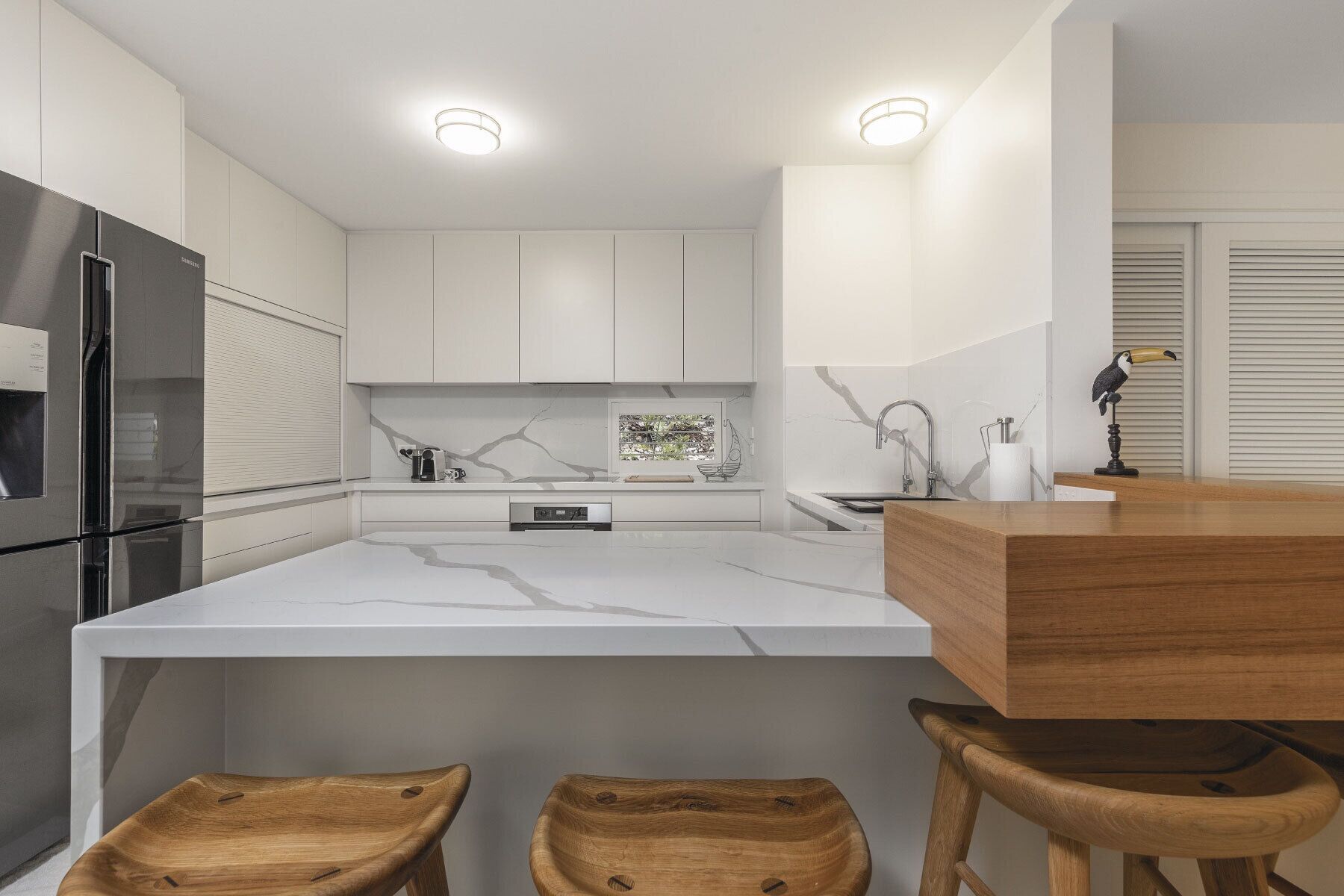 Une cuisine moderne avec des meubles blancs, un grand îlot central et des tabourets en bois.