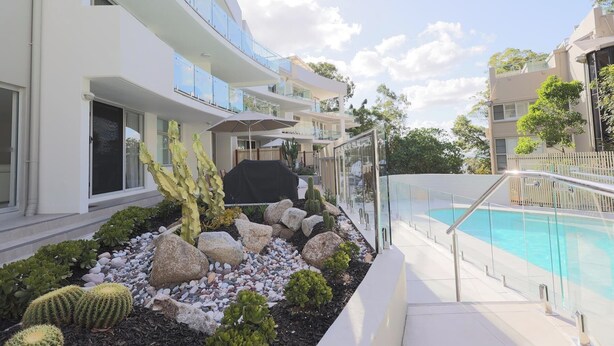 A modern hotel with a pool area, featuring a glass railing, a cactus garden, and a multi-story building with balconies. - Apartment 3 - The Cove (Noosa Heads)