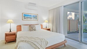 A hotel room with a large bed, two bedside tables with lamps, a window with curtains, and a picture on the wall. - Apartment 3 - The Cove (Noosa Heads)