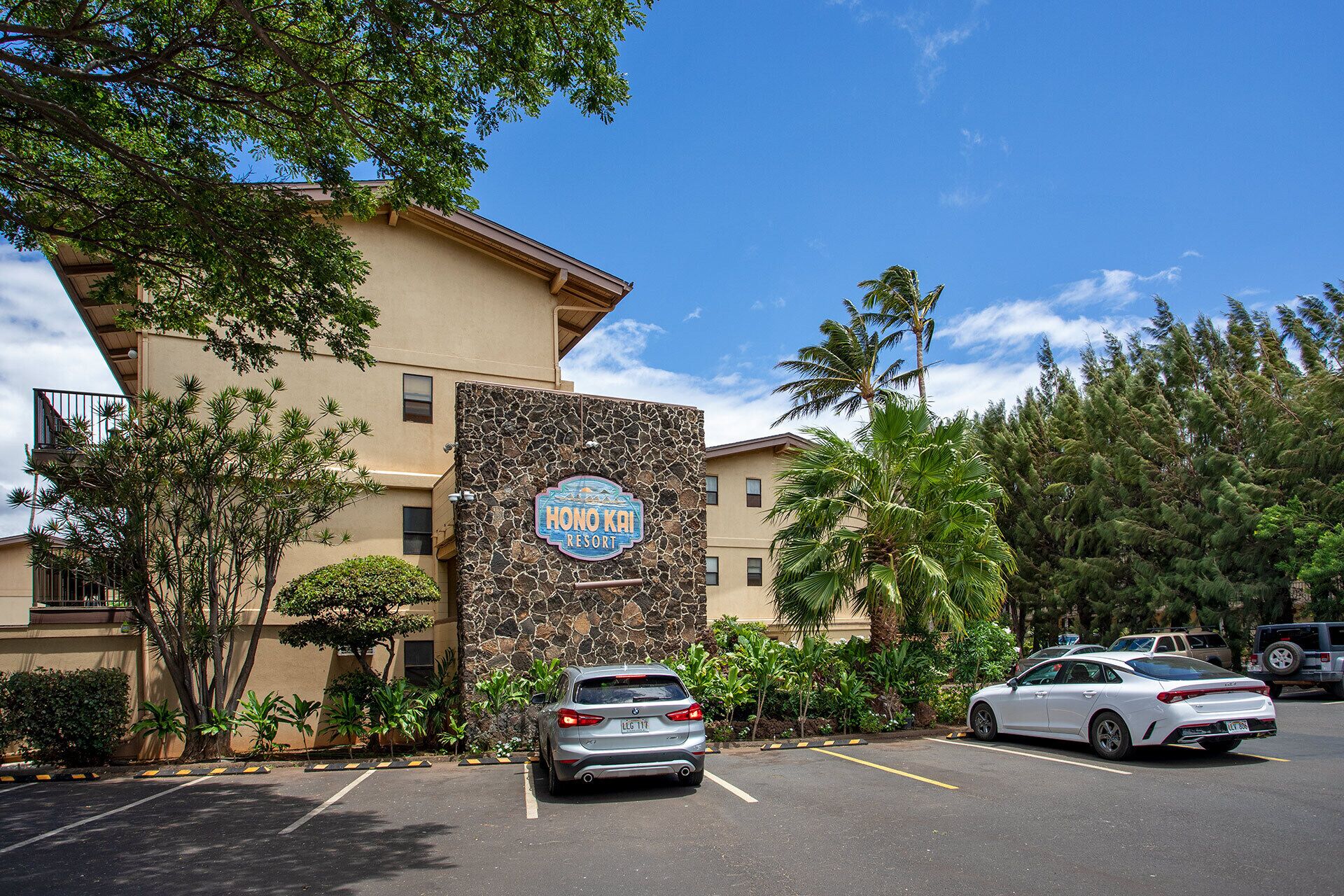 Un hôtel appelé « Honolulu Resort », doté d’une façade en pierre, d’un parking et entouré de verdure.