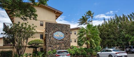 Un hôtel appelé « Honolulu Resort », doté d’une façade en pierre, d’un parking et entouré de verdure.
