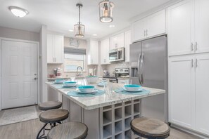 Una cocina moderna con armarios blancos, electrodomésticos de acero inoxidable y una isla central con taburetes.