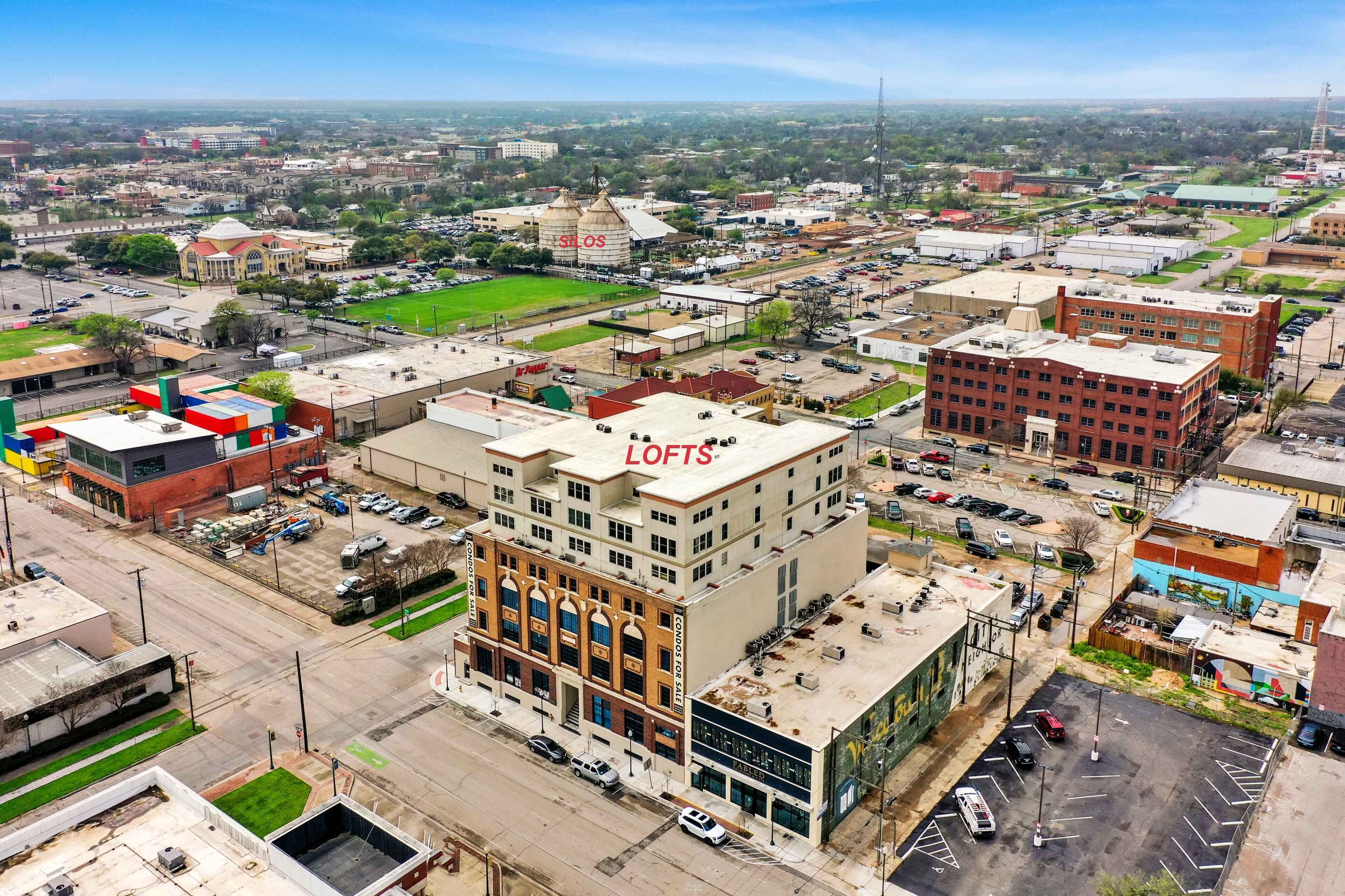 A multi-story building with a prominent 'LOFTS' sign on the roof, surrounded by parking lots and other buildings.