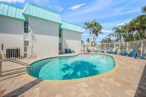 A swimming pool with a white building, palm trees, and blue chairs.