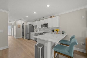 A modern kitchen with white cabinets, stainless steel appliances, and a central island with seating. - Steps to Siesta Key Village, Walk to Beach (Siesta Key)