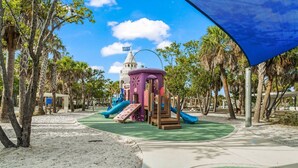 Un'area giochi con scivoli e strutture per arrampicarsi, circondata da palme e un cielo sereno.