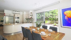 A modern kitchen with white cabinets, a built-in oven, and a refrigerator. There is a dining area with a wooden table set for four, surrounded by black chairs.