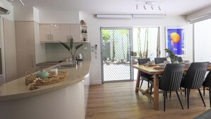 A modern kitchen with a dining area, featuring a wooden dining table, black chairs, and a large window with a view of greenery.