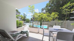 A patio area with a pool, white lounge chairs, and a table with chairs.