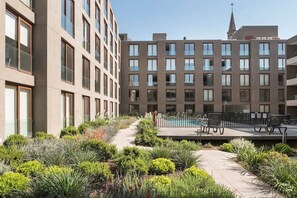 Un edificio moderno con varios pisos, un área de piscina con sillones reclinables y un jardín bien cuidado.