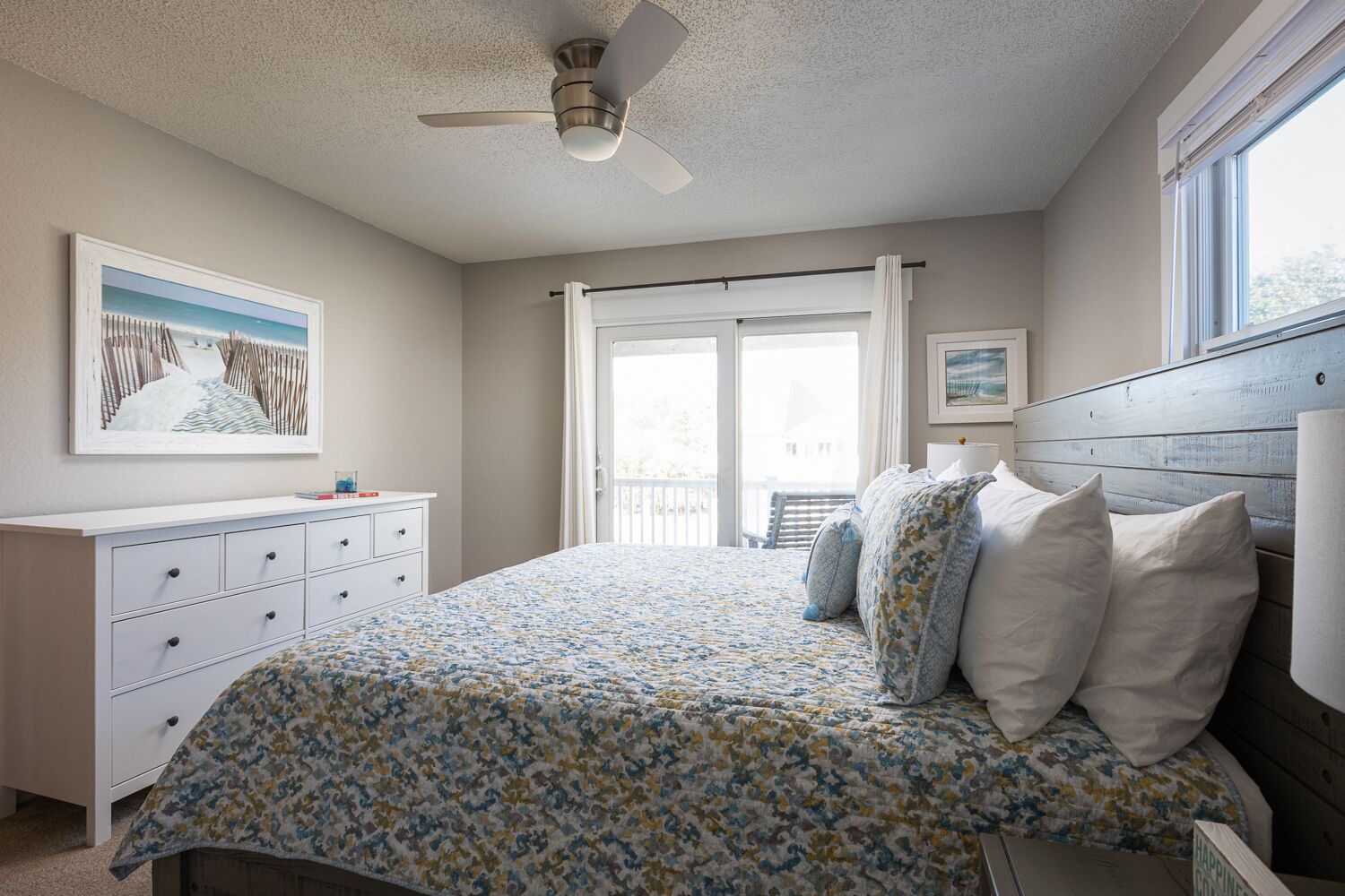 A bedroom with a bed, a dresser, a ceiling fan, and a window.