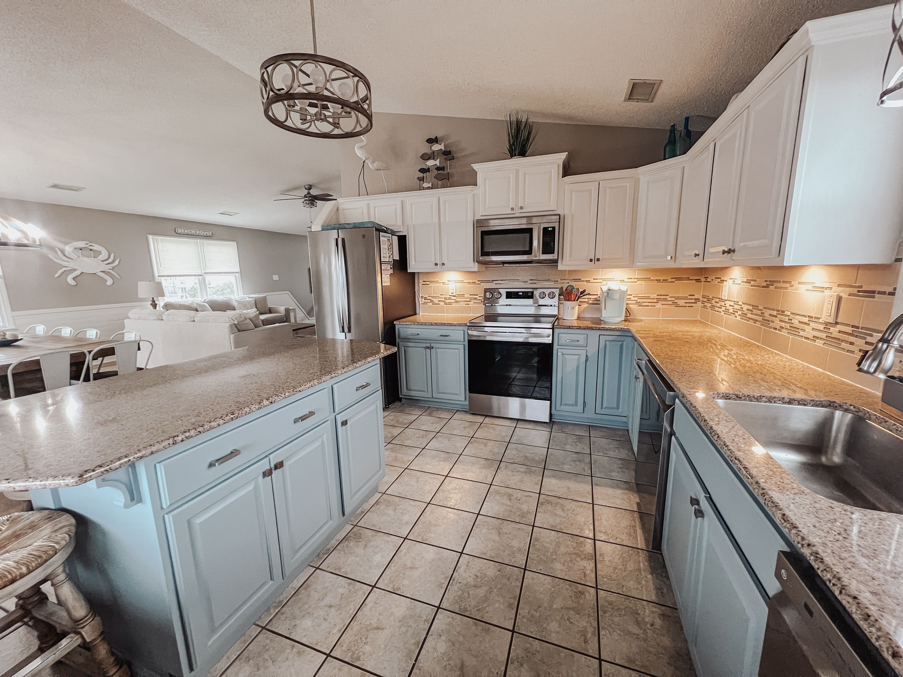 A modern kitchen with light blue cabinets, a stainless steel refrigerator, a microwave, and a built-in oven.