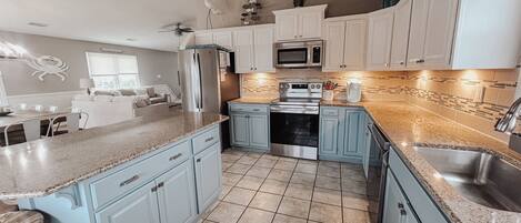 A modern kitchen with light blue cabinets, a stainless steel refrigerator, a microwave, and a built-in oven.