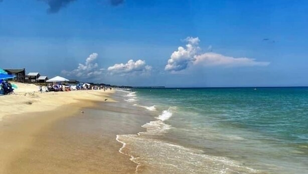 Een strand met helder water, een zandstrand en enkele parasols.