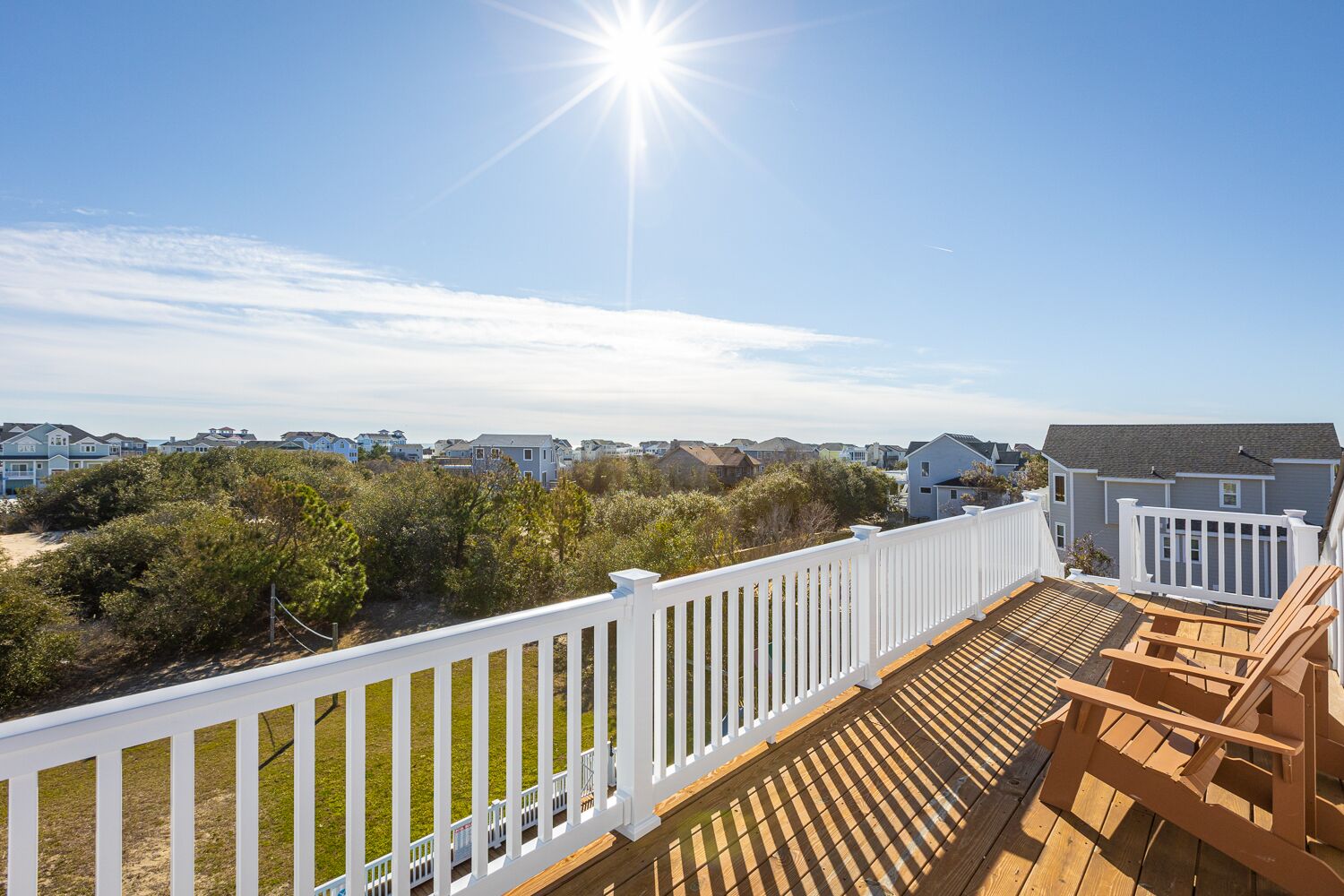 A wooden deck with a white railing overlooking a residential area with houses and greenery.