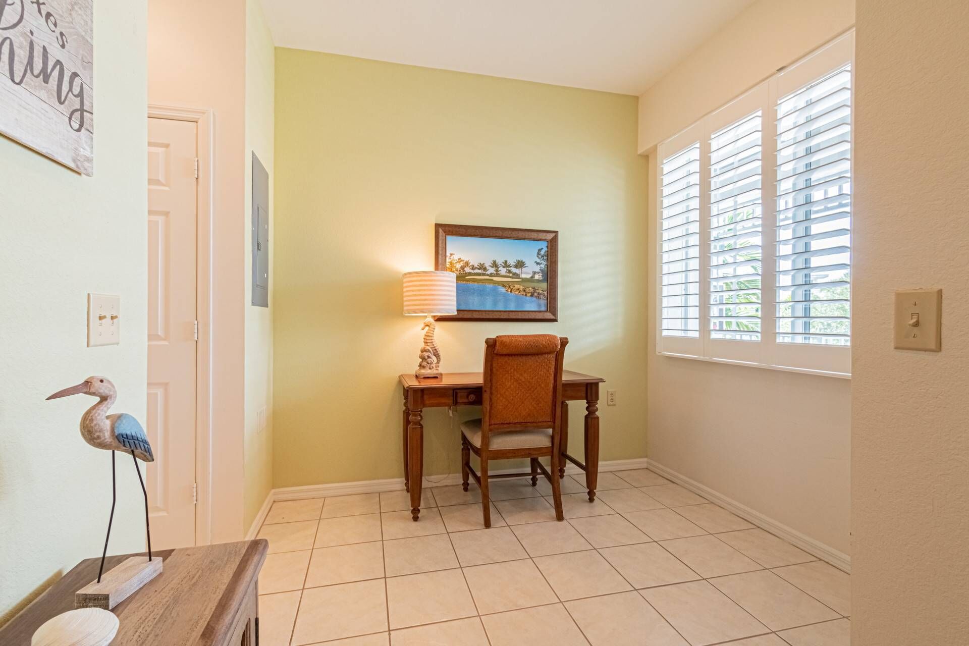 A room with a desk, chair, lamp, and a painting on the wall.