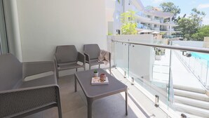 Un balcon avec deux chaises et une table, une balustrade en verre et une vue sur un immeuble et des arbres.