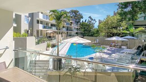 Un moderno edificio residenziale con piscina sul tetto, ringhiere in vetro e area relax all'aperto.