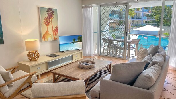 Un soggiorno moderno con TV, divano e zona pranzo con vista su una piscina.
