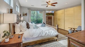 A bedroom with a large bed, a ceiling fan, a TV, and a view of the outdoors. - Experience luxury in this 3-bedroom home with stunning red rock views in Sedona. (Sedona)