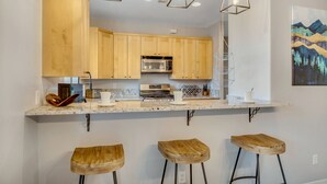 A kitchen with wooden cabinets, a stainless steel microwave, a coffee machine, and three wooden stools. - Experience luxury in this 3-bedroom home with stunning red rock views in Sedona. (Sedona)
