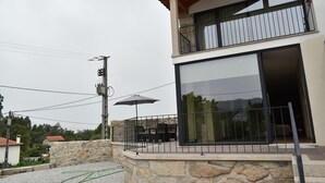 Une maison moderne à deux étages, dotée d’un balcon, de murs en pierre et d’une grande porte-fenêtre coulissante.