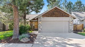 A residential house with a stone facade, a garage, and a well-maintained lawn. - Quail Covey - Hot Tub, AC, Beautiful, Fully Fenced Yard, Close to Everything! (Bend)