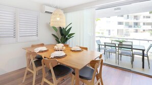 A dining area with a wooden table, chairs, and a hanging light fixture. - Apartment 7 - The Cove (Noosa)