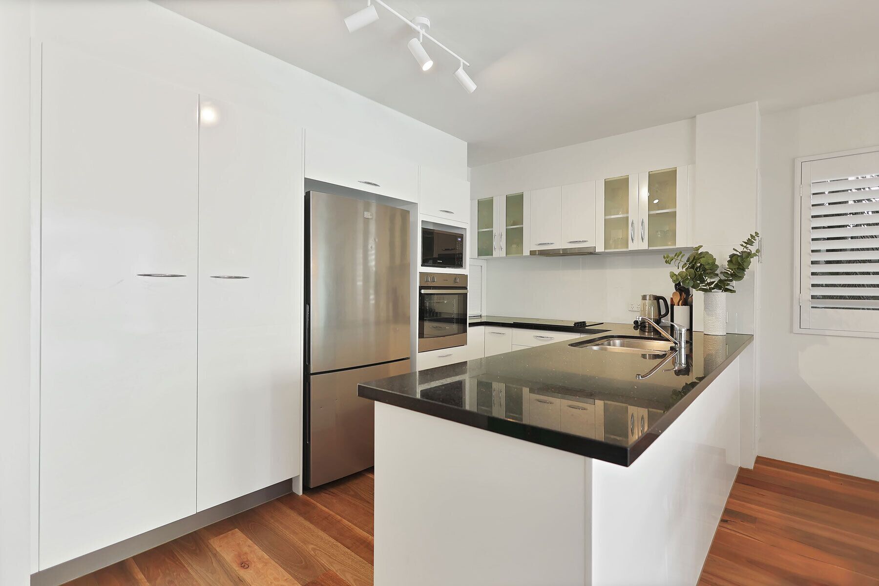 Een moderne keuken met witte kasten, roestvrijstalen apparatuur en een houten vloer.