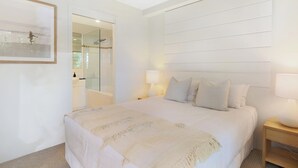 A bedroom with a large bed, two bedside lamps, a nightstand, a mirror, and a framed picture on the wall. - Apartment 7 - The Cove (Noosa)
