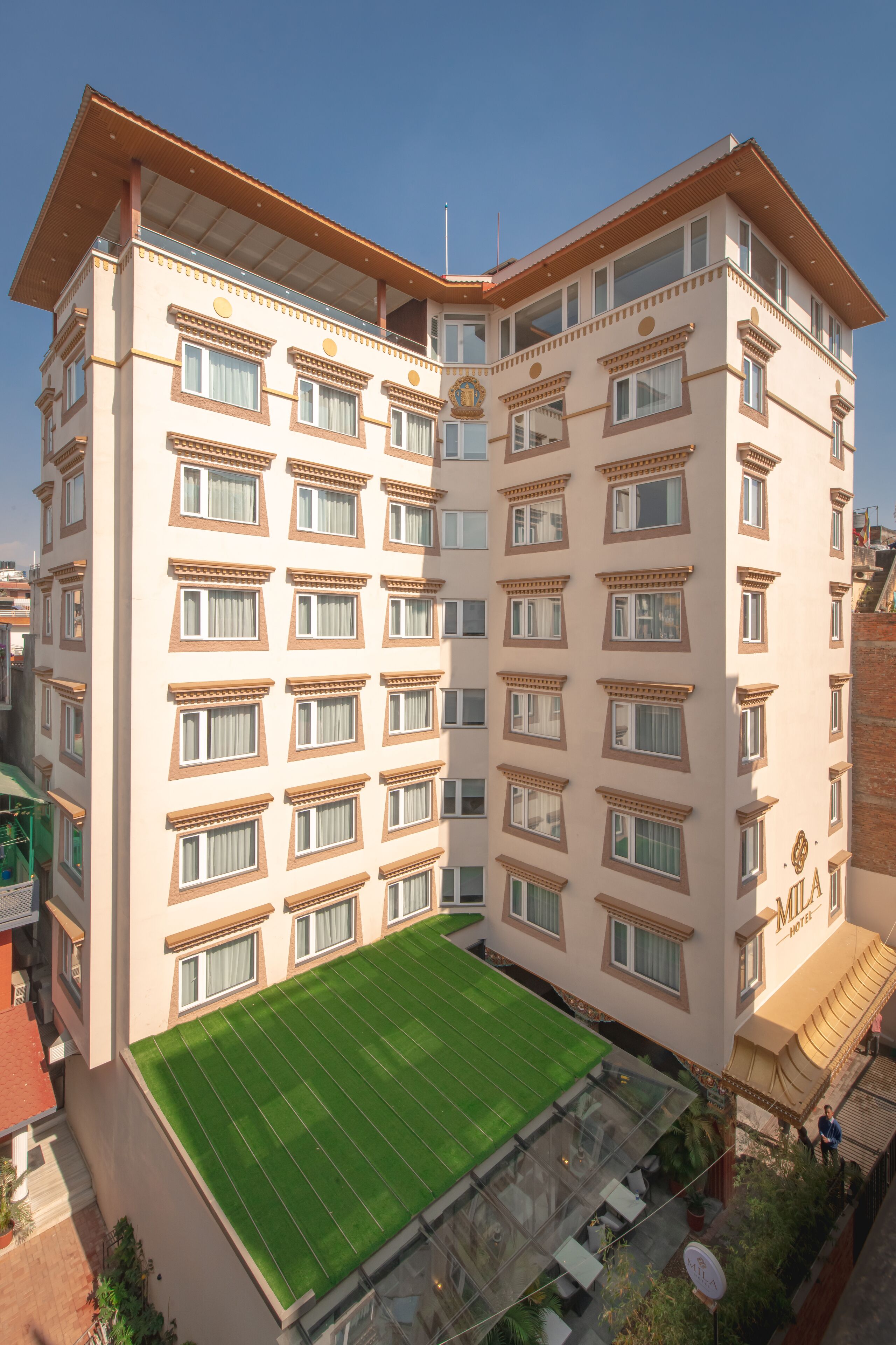 A multi-story hotel with a green rooftop terrace, multiple windows, and a visible entrance.