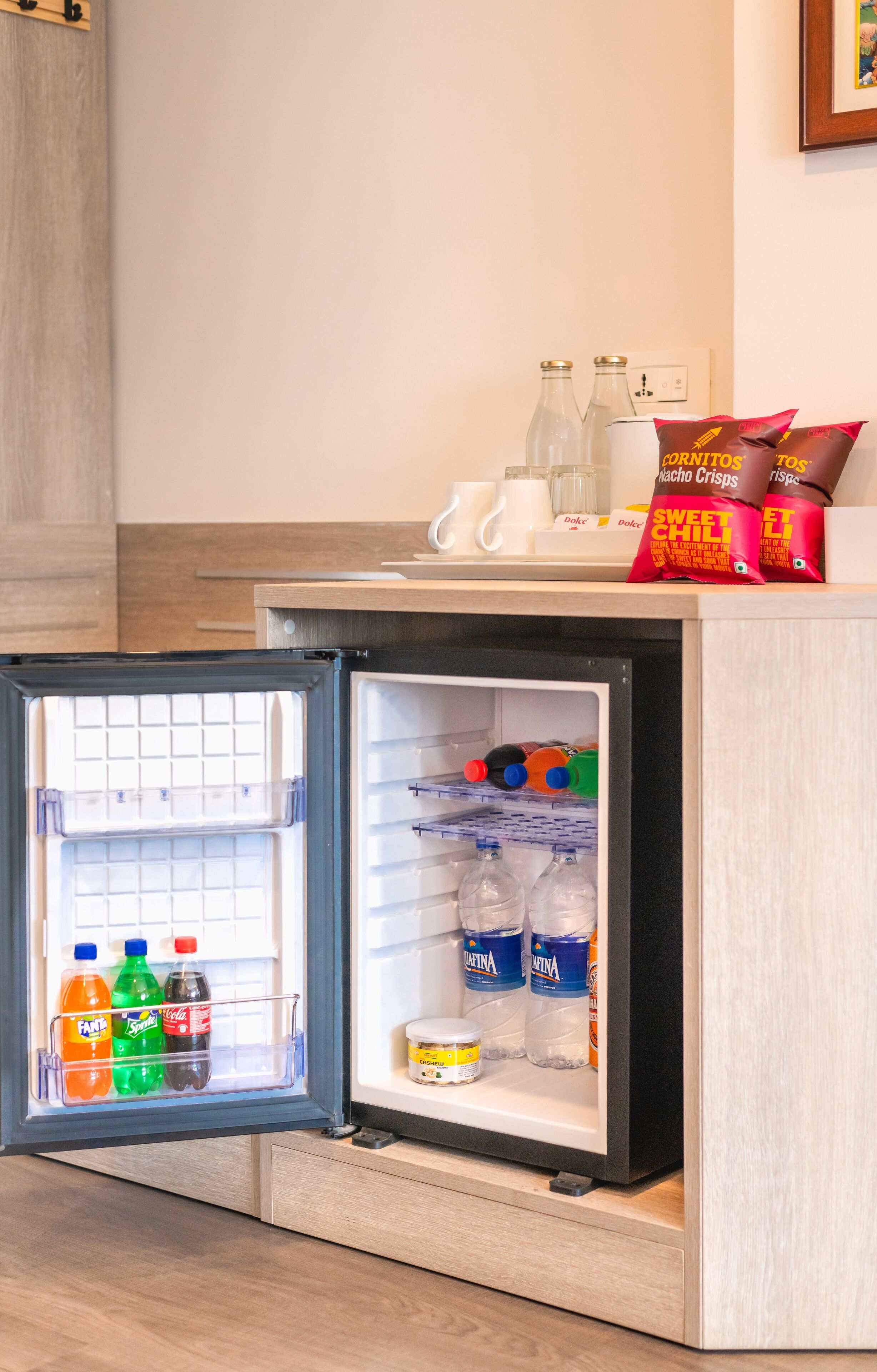 A compact refrigerator with a freezer compartment on the left and a main compartment on the right. The freezer contains several bottles of water and a jar of peanut butter. The main compartment has shelves with bottles of water, a jar of peanut butter, and a bag of Doritos chips.