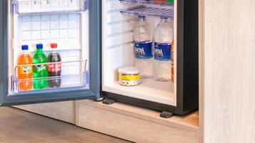A compact refrigerator with a freezer compartment on the left and a main compartment on the right. The freezer contains several bottles of water and a jar of peanut butter. The main compartment has shelves with bottles of water, a jar of peanut butter, and a bag of Doritos chips.