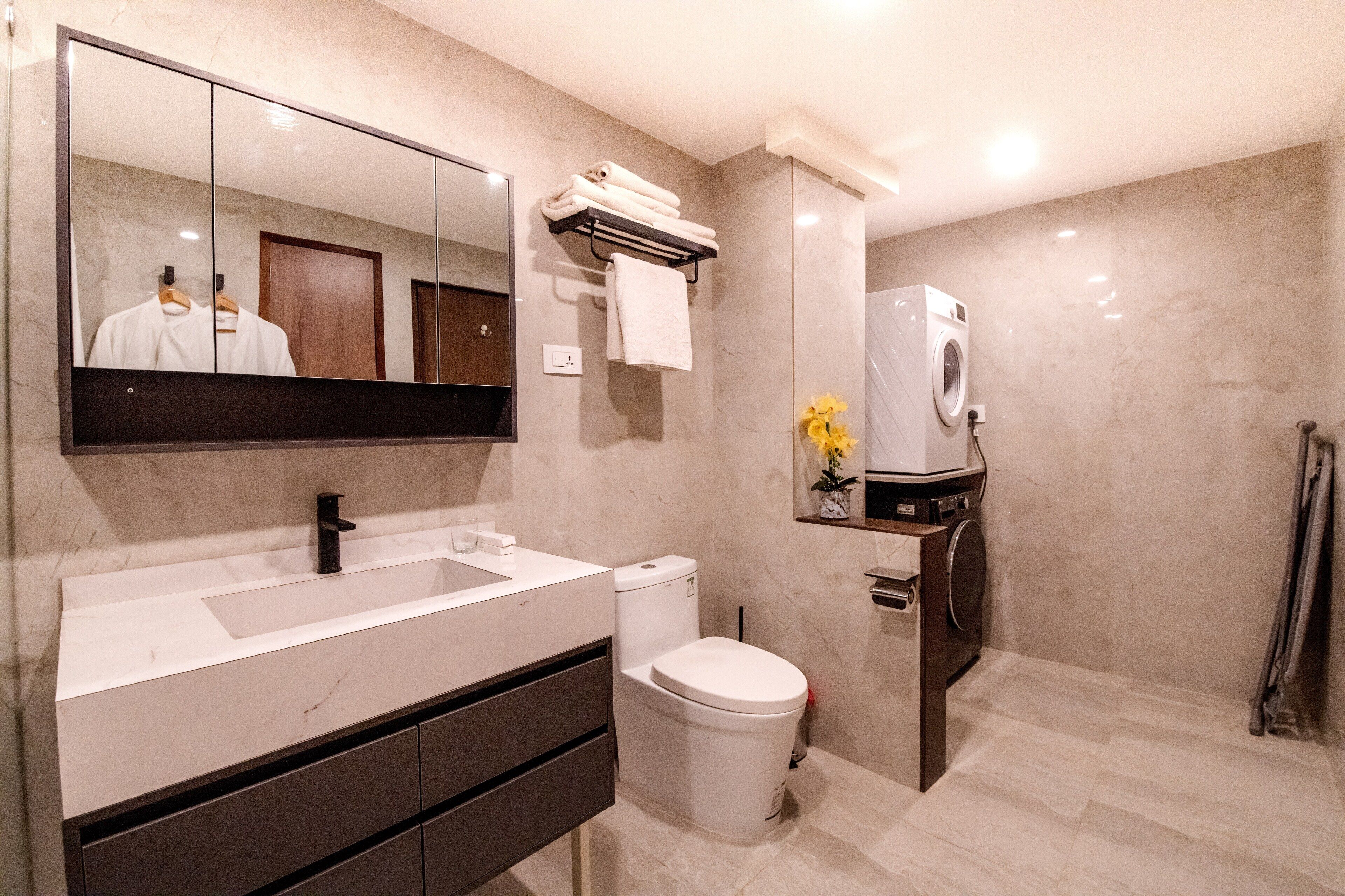 A modern bathroom with a large mirror, a white sink, a toilet, and a built-in washing machine.