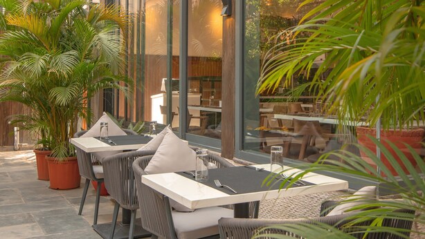 An indoor patio area with tables and chairs, surrounded by potted plants and a glass ceiling. - Mila Hotel (Kathmandu)