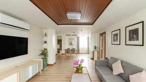 A modern living room with a flat-screen TV, a grey sofa, a wooden coffee table, and a dining area in the background. - Mila Hotel (Kathmandu)