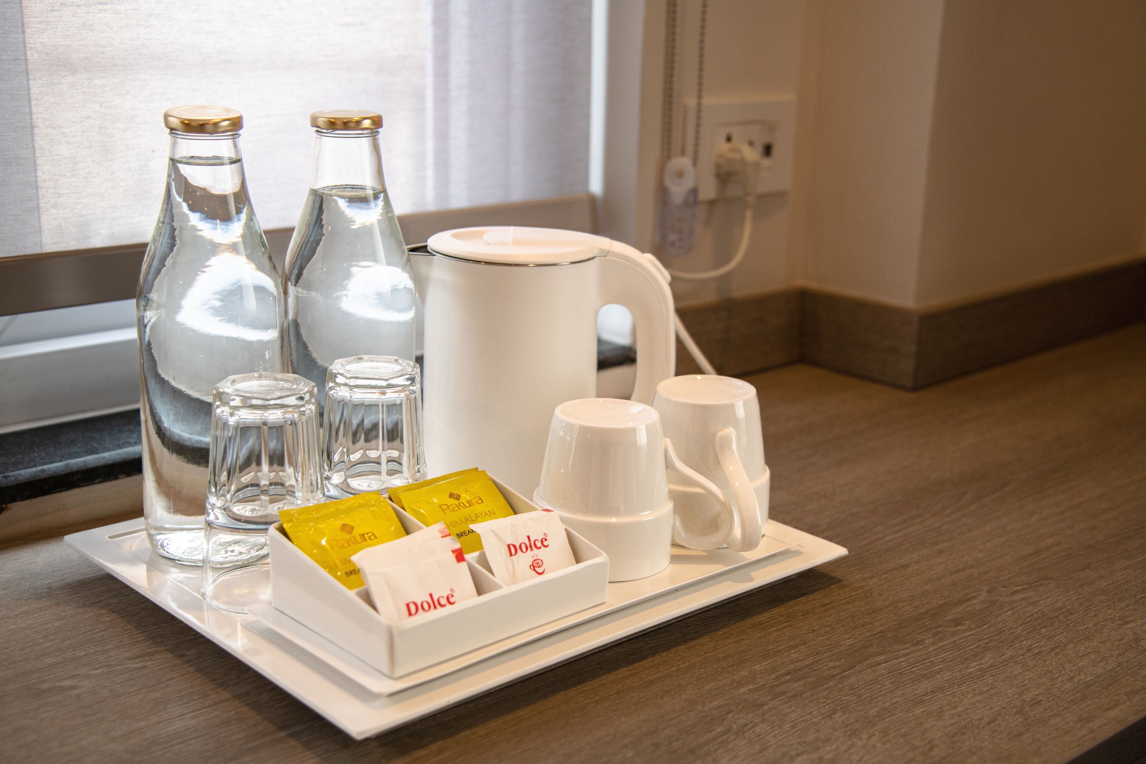 A tray with glass bottles, a white coffee maker, and a box of Dolce de la Vina chocolates.