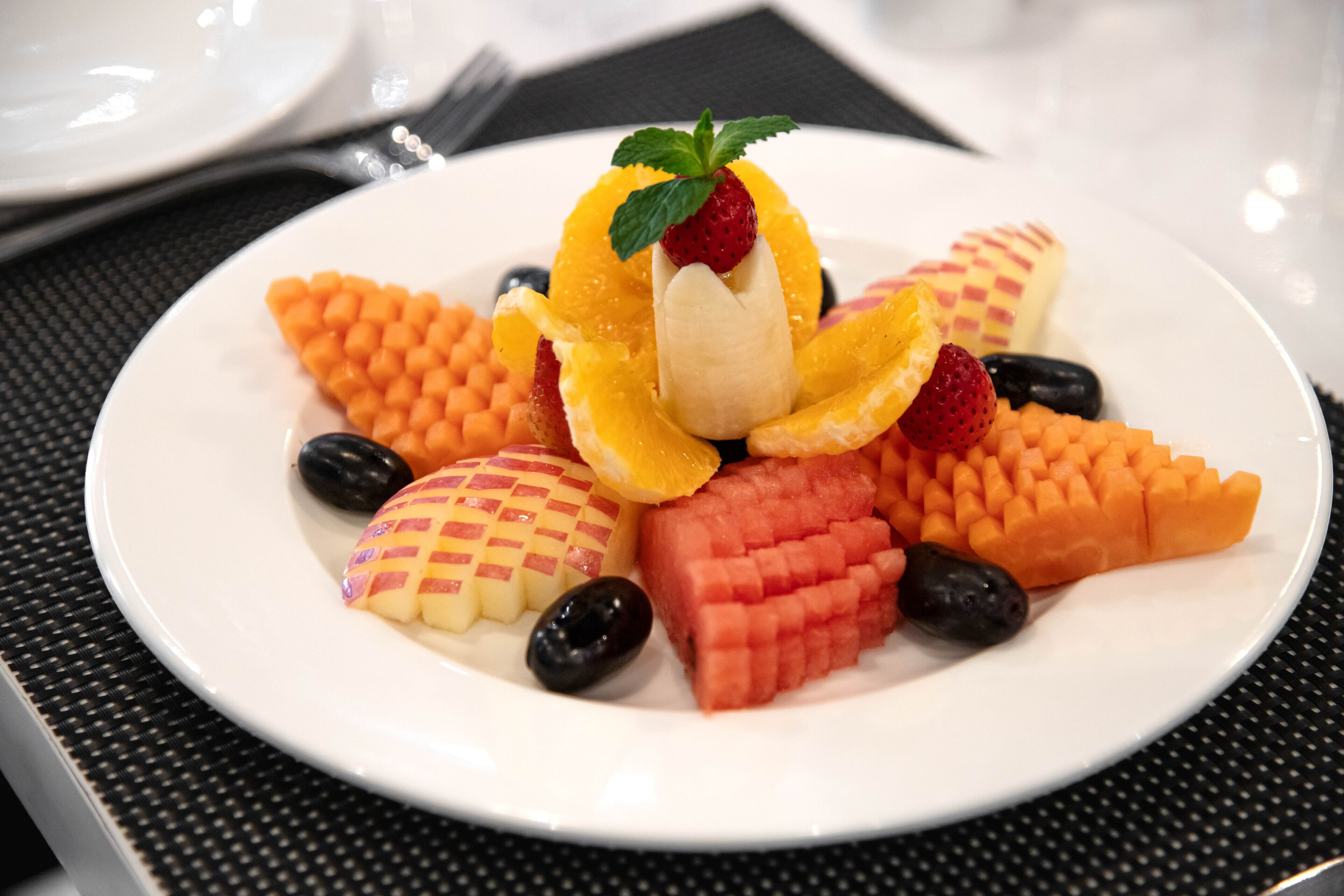 A white plate with various fruits and a strawberry on top, placed on a black textured tablecloth.