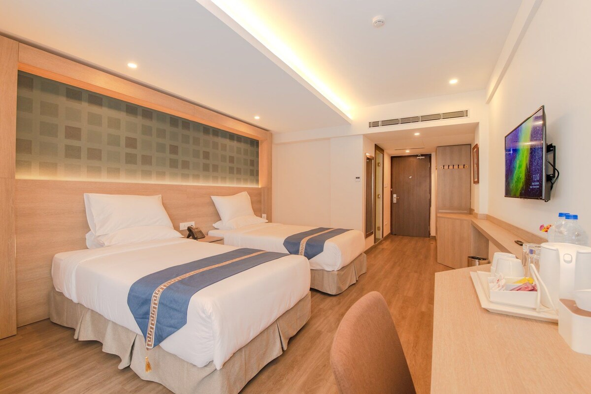 A hotel room with two beds, a desk with amenities, a TV, and a bathroom door.