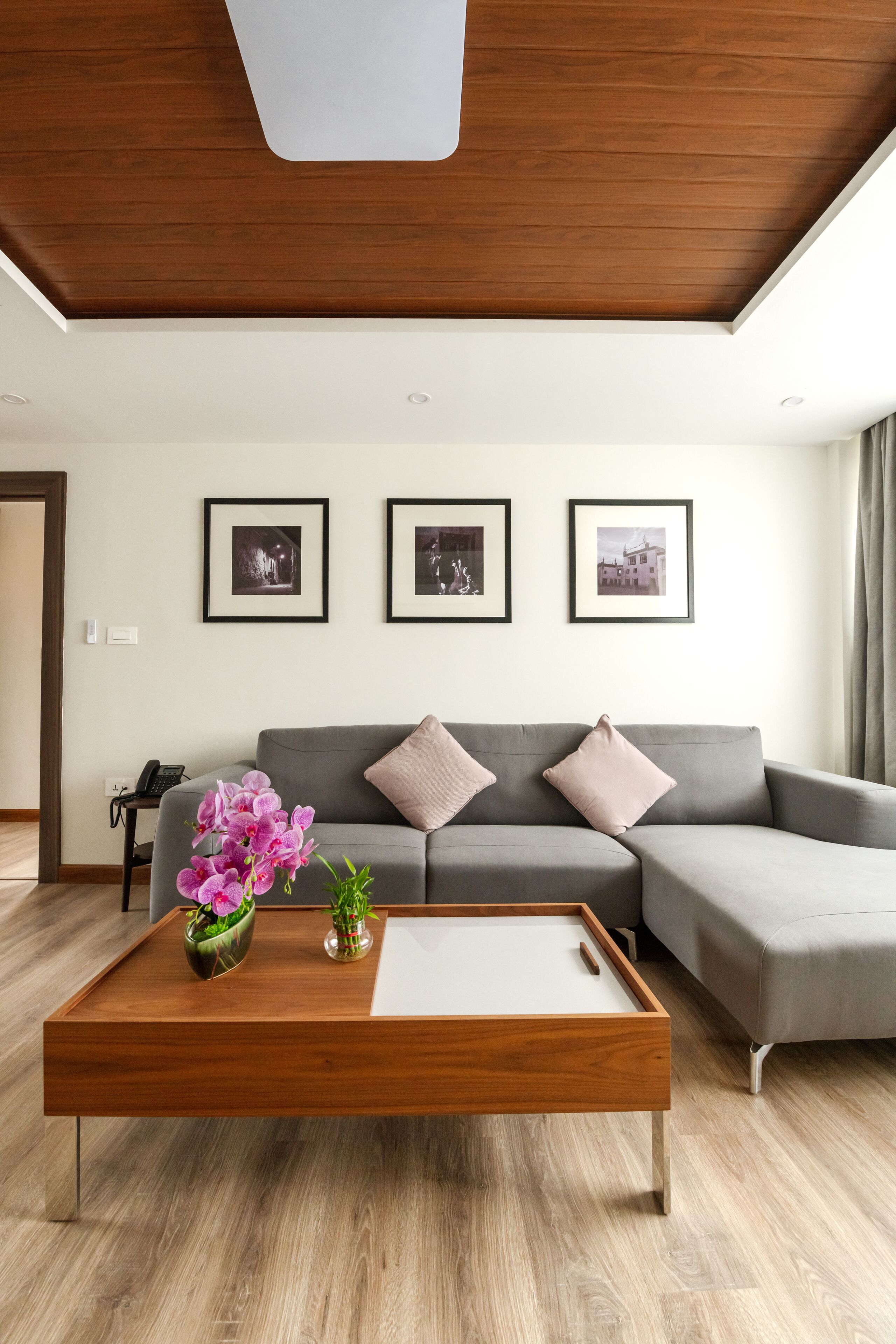 A modern living room with a grey sofa, a wooden coffee table with a vase of flowers, and framed pictures on the wall.