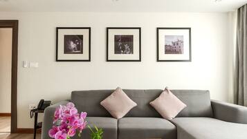A modern living room with a grey sofa, a wooden coffee table with a vase of flowers, and framed pictures on the wall.