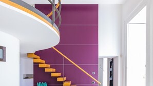 A modern interior with a spiral staircase, a glass dining table, and a purple accent wall.