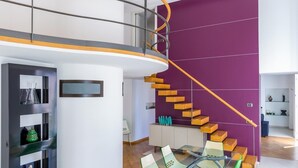 A modern interior with a spiral staircase, a glass dining table with green chairs, and a wooden ceiling.