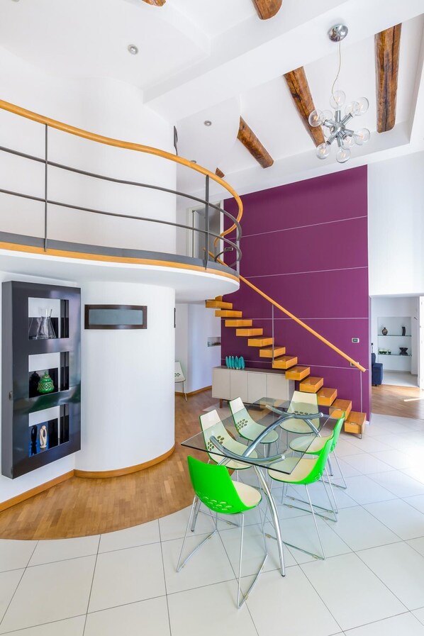 Ein modernes Interieur mit einer Wendeltreppe, einem Glastisch mit grünen Stühlen und einer Holzbalkendecke.