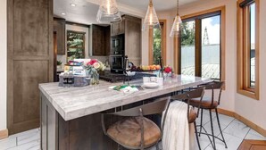 Una cocina moderna con encimera de mármol, lámparas colgantes y una isla central con taburetes de bar.