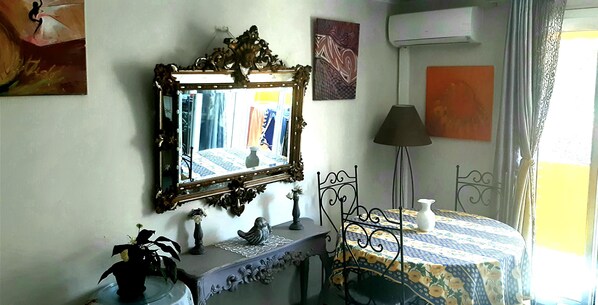 A room with a mirror, a table with a patterned tablecloth, a lamp, and decorative items on a console table.