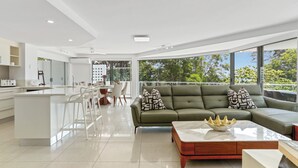 A modern living room with a sofa, coffee table, and dining area. - Penthouse 9 - The Cove (Noosa Heads)