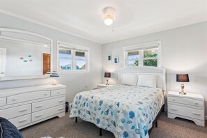 Ein Schlafzimmer mit einem Bett, zwei Nachttischen, einer Kommode, einem Fenster und einer Deckenleuchte.